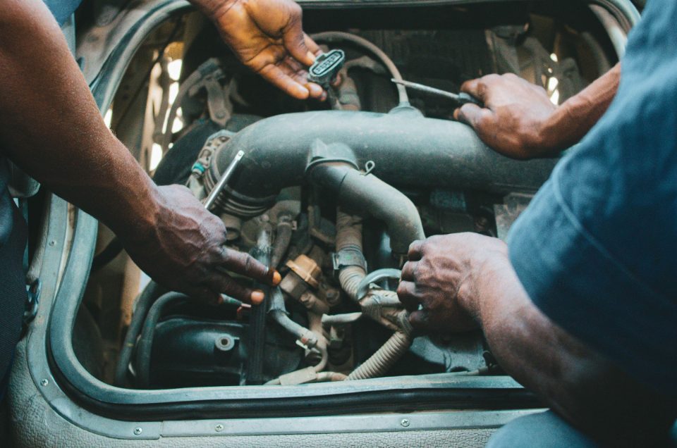 Close-up of two mechanics' hands working together on an engine, one holding a wiring connector and the other a ratchet