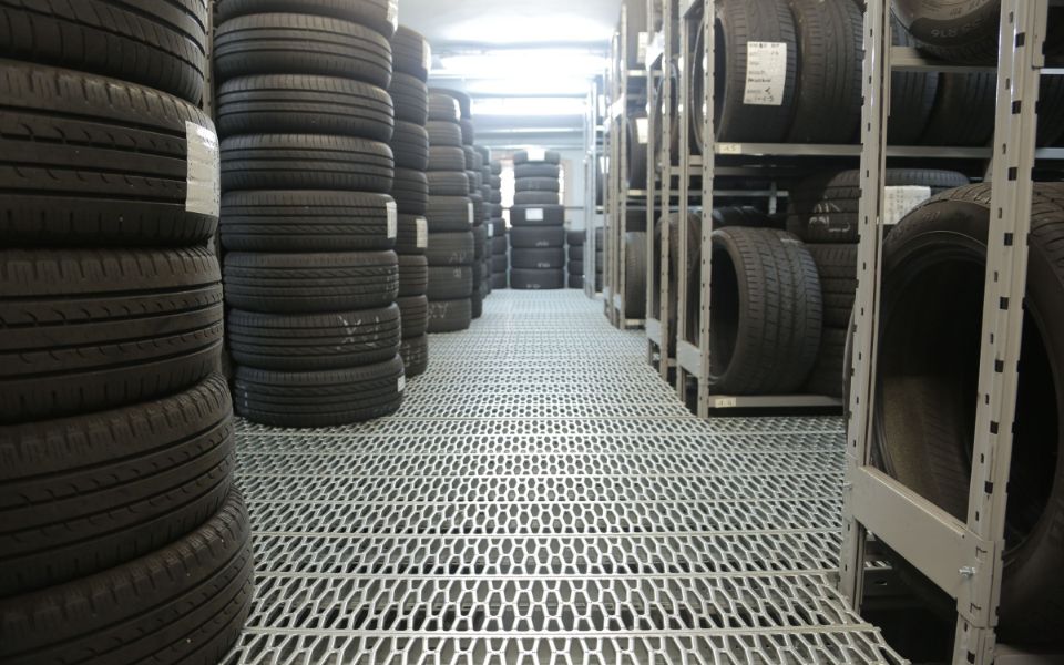 Tall stacks of tires and tagged tire racks along a clean, bright storage aisle